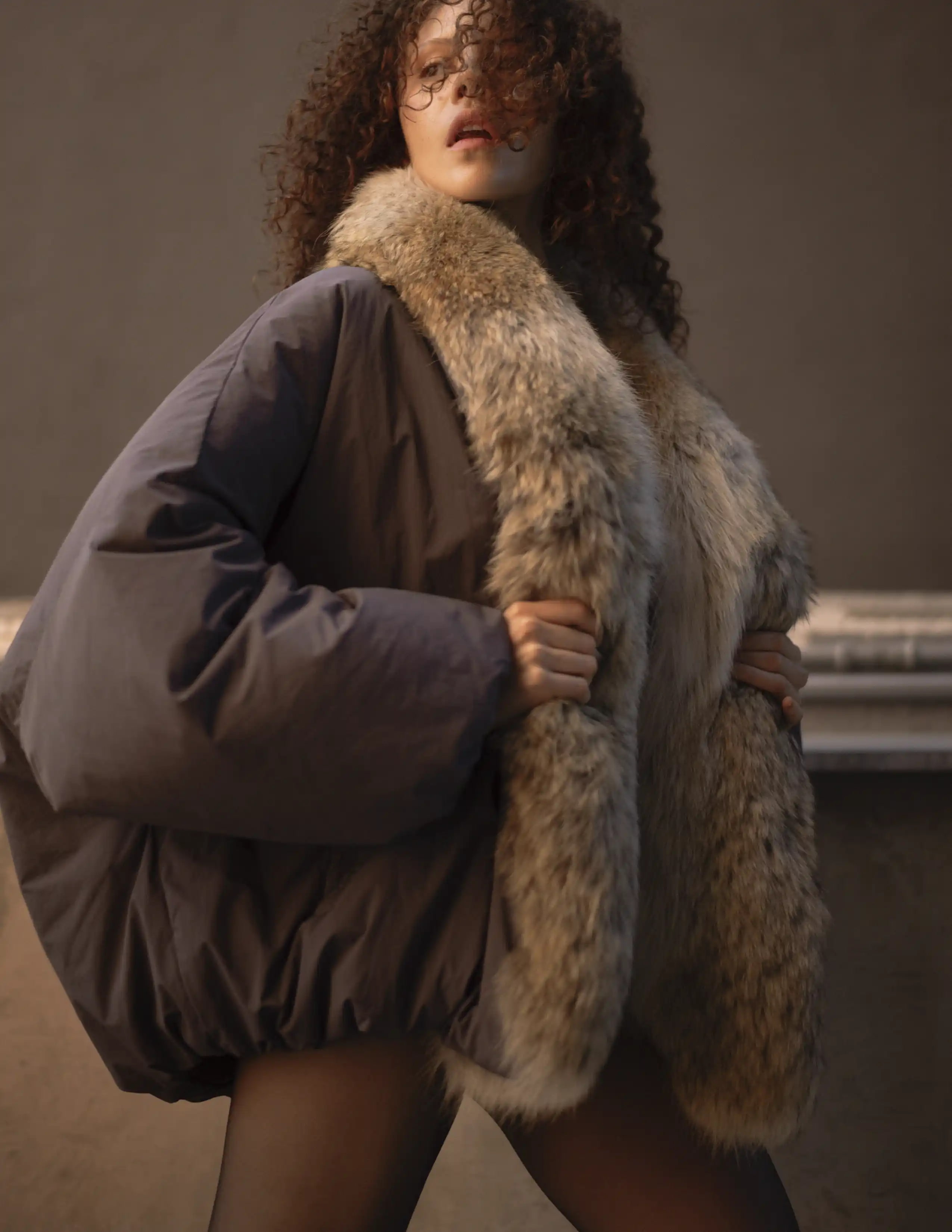 Modelo con abrigo oversized de piel sintética y mangas voluminosas en tonos grises, moda invierno editorial.
